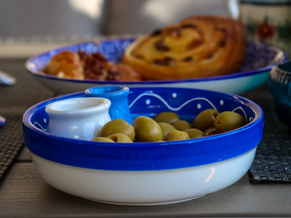 Πράσινες ελιές και ένα μικρό κανάτι ελαιόλαδο σε γαλανόλευκο κεραμικό σκεύος.